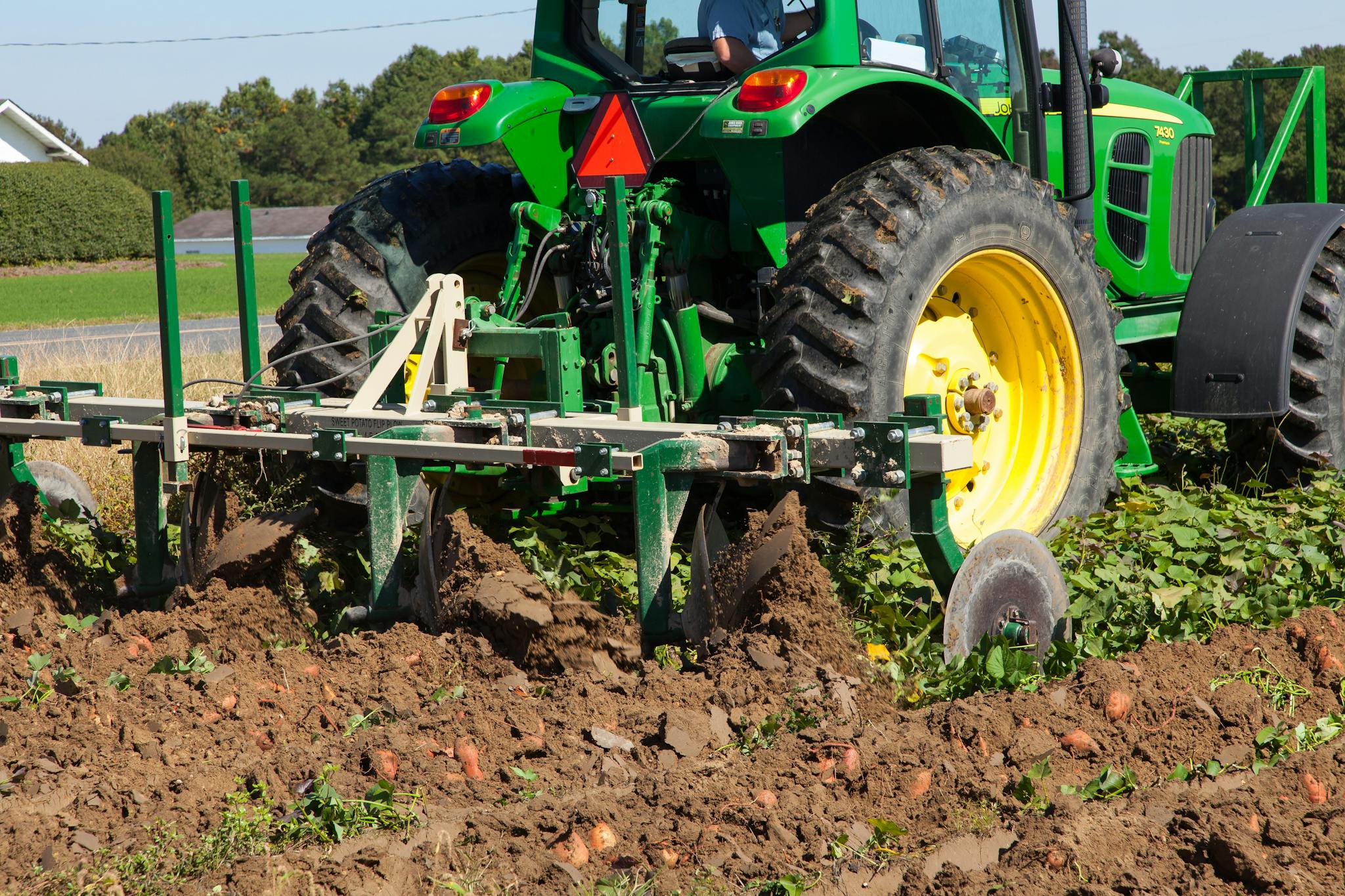 A green tractor plowing a field in North Carolina during summer. Agriculture machinery and crops visible.